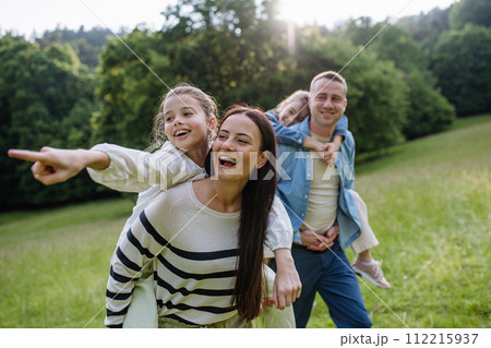 Portrait of beautiful family, parents piggibacking two daughters, having fun in nature. 112215937