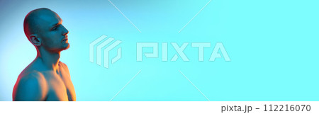 Side view portrait of handsome young bald man posing shirtless against blue studio background in neon light 112216070