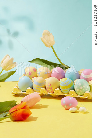 Easter joy captured in picturesque frame. The colorful and patterned eggs are arranged in a blister decorated with tulips on pastel color background. Idea for Easter decoration 112217109