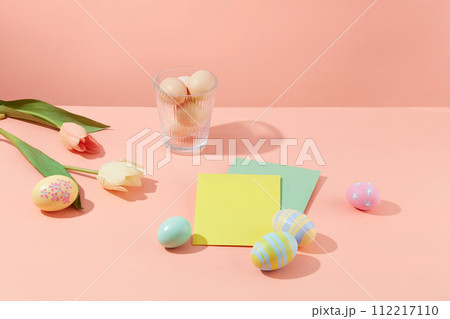 Scene of colorful eggs decorated with flowers and paper card on a pastel pink background. Make your own Easter eggs as meaningful gifts 112217110