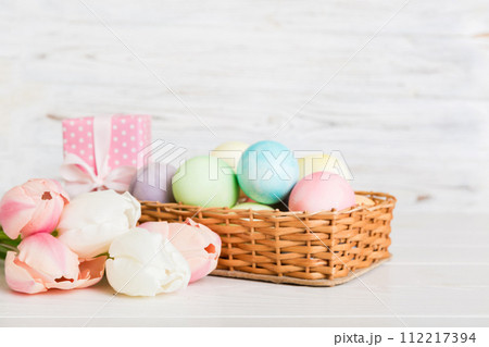 Happy Easter composition. Easter eggs in basket on colored table with yellow Tulips. Natural dyed colorful eggs background with copy space Happy Easter composition. Easter eggs in basket on colored table with yellow Tulips. Natural dyed colorful eggs background with copy space 112217394