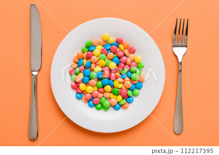 cutlery on table and sweet plate of candy. Health and obesity concept, top view on colored background cutlery on table and sweet plate of candy. Health and obesity concept, top view on colored background 112217395