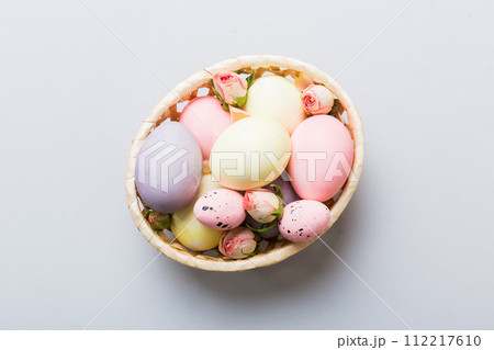 Happy Easter. Easter eggs in basket on colored table with yellow roses. Natural dyed colorful eggs background top view with copy space Happy Easter. Easter eggs in basket on colored table with yellow roses. Natural dyed colorful eggs background top view with copy space 112217610
