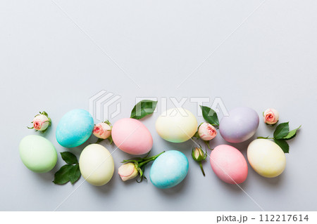 Happy Easter. Easter eggs on colored table with yellow roses. Natural dyed colorful eggs background top view with copy space Happy Easter. Easter eggs on colored table with yellow roses. Natural dyed colorful eggs background top view with copy space 112217614