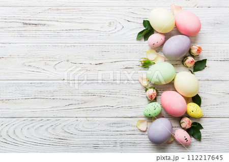 Happy Easter. Easter eggs on colored table with yellow roses. Natural dyed colorful eggs background top view with copy space 112217645