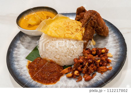 Asian food Nasi Lemak is a rice dish infused with coconut milk. Served with sambal, fried chicken wing, fried peanut, fried egg with curry sauce. Asian food Nasi Lemak is a rice dish infused with coconut milk. Served with sambal, fried chicken wing, fried peanut, fried egg with curry sauce. 112217802