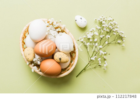 Happy Easter composition. Easter eggs in basket on colored table with gypsophila. Natural dyed colorful eggs background top view with copy space Happy Easter composition. Easter eggs in basket on colored table with gypsophila. Natural dyed colorful eggs background top view with copy space 112217848