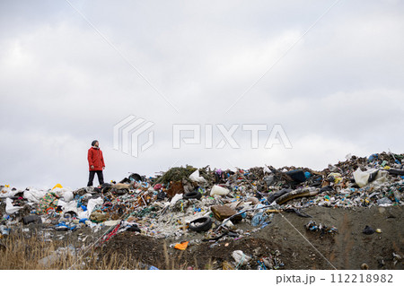 Activist standing on landfill, on large pile of waste with dark clouds above. Environmental concept and eco activism. 112218982