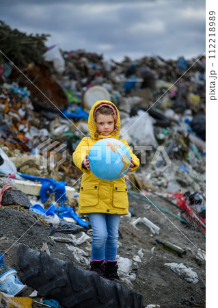 Young girl holding planet Earth model, globe, standing standing on landfill, large pile of waste, nature pollution environmental concept and eco activism. Young girl holding planet Earth model, globe, standing standing on landfill, large pile of waste, nature pollution environmental concept and eco activism. 112218989