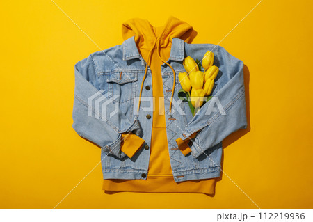 Hoodie, jeans jacket and flowers on yellow background, top view 112219936