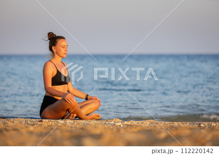 Fitness woman breathing and meditating near the sea at sunset Fitness woman breathing and meditating near the sea at sunset 112220142