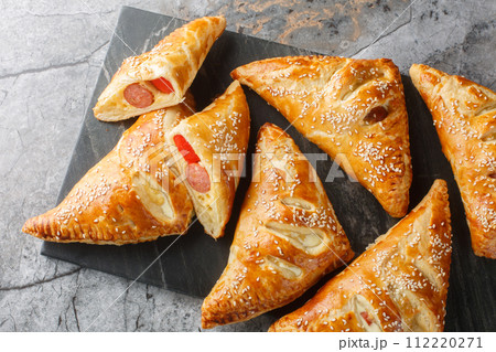 Delicious puff pastry pies with sausage, cheese, sesame and pepper close-up on a marble board. Horizontal top view 112220271