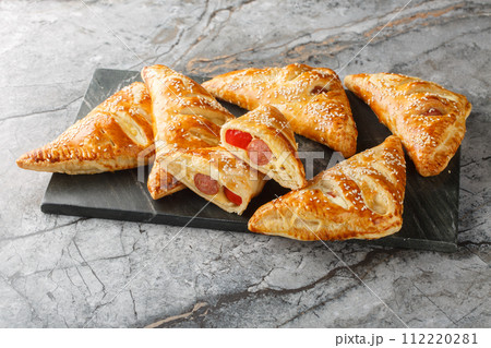 Delicious puff pastry pies with sausage, cheese, sesame and pepper close-up on a marble board. Horizontal 112220281
