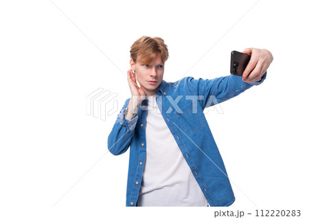 young man with red hair in a blue shirt takes a selfie on the phone 112220283