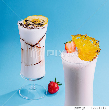 two glass cups of milkshake with dry pineapple and strawberries two glass cups of milkshake with dry pineapple and strawberries 112221515