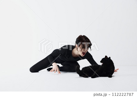 Artistic beautiful woman in emotional stance with black cat, both displaying dynamic expressions of anger, shouting against white studio background. 112222787