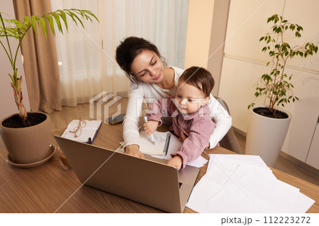 Cheerful pretty businesswoman working at home with her little child girl 112223272