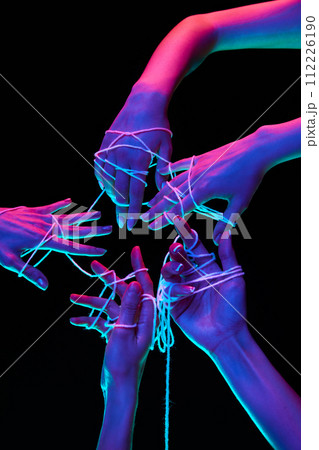 Hands joined with white thread makes star shape and symbolize global communication in multicolored neon lighting against black studio background. 112226190