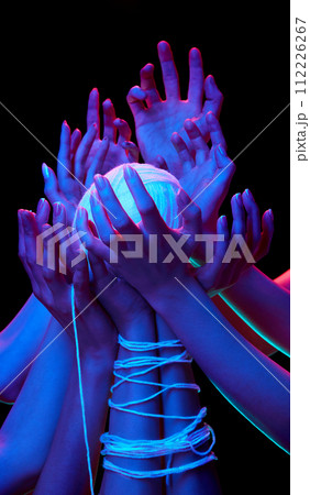 Hands encircle glowing ball of threads in multicolored neon lighting against black studio background, symbolizing global unity. 112226267