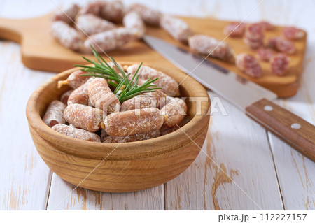 Mini salami sausages in a bowl on a white wooden table. 112227157