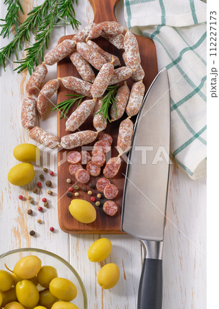 Mini salami sausages with rosemary and olives on a wooden cutting board, top view. Mini salami sausages with rosemary and olives on a wooden cutting board, top view. 112227173