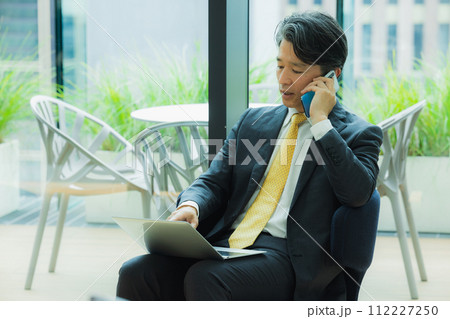 オフィスでスマホで通話するビジネスマン オフィスでスマホで通話するビジネスマン 112227250