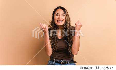Happy hispanic woman celebrating raising fists and looking at camera 112227957