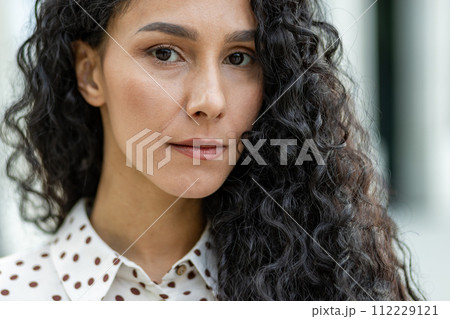Close-up of an elegant curly-haired woman in a stylish polka-dot blouse. The image captures a fashionable female detail, perfect for beauty and fashion themes. 112229121