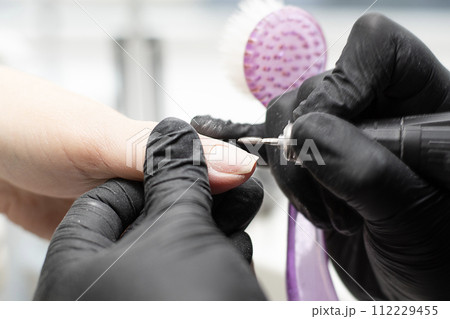 Beauty concept. A manicurist in black latex gloves makes a hygienic hardware manicure with a Fraser to a client in a beauty salon. 112229455