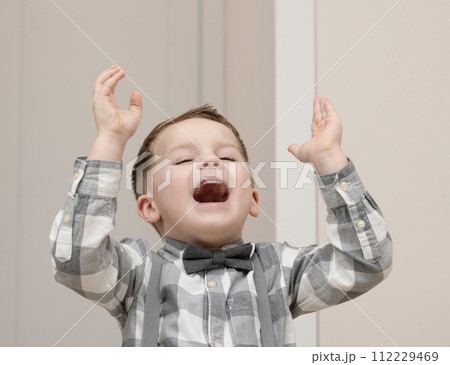 Emotions of happiness, fun, joy and delight on the child s face. A small handsome boy of 4 years old in a shirt with a bow tie shows a mime with a facial expression. Emotions of happiness, fun, joy and delight on the child s face. A small handsome boy of 4 years old in a shirt with a bow tie shows a mime with a facial expression. 112229469