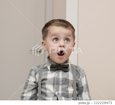 Emotions of surprise and delight on the child s face. A small handsome boy of 4 years old in a shirt with a bow tie shows a grimace with an expression on his face. Close-up. Emotions of surprise and delight on the child s face. A small handsome boy of 4 years old in a shirt with a bow tie shows a grimace with an expression on his face. Close-up. 112229473