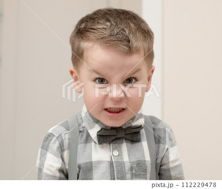 Emotions of anger and anger on a child's face. A small handsome boy, 4 years old, wearing a shirt with a bow tie, shows a grimace with facial expressions. Emotions of anger and anger on a child's face. A small handsome boy, 4 years old, wearing a shirt with a bow tie, shows a grimace with facial expressions. 112229478