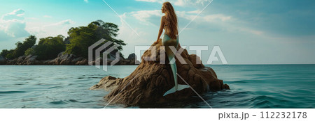Young mermaid sitting on a rock on an island in the sea. 112232178