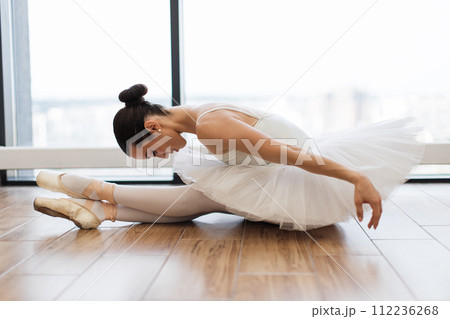 Graceful woman ballet dancer stretching while sitting on wooden floor. Graceful woman ballet dancer stretching while sitting on wooden floor. 112236268