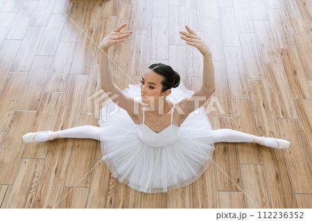 Professional ballerina in tutu and pointe stretching on floor. 112236352