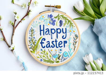 Happy Easter embroidered text on light background with spring flowers. 112237413