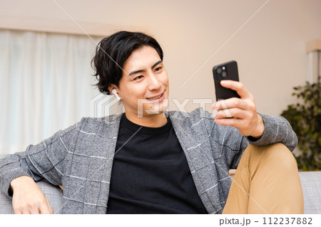 スマートフォンで音楽を聞きワイヤレスイヤフォンで通話しゲームを楽しむ笑顔の30代の男性 スマートフォンで音楽を聞きワイヤレスイヤフォンで通話しゲームを楽しむ笑顔の30代の男性 112237882