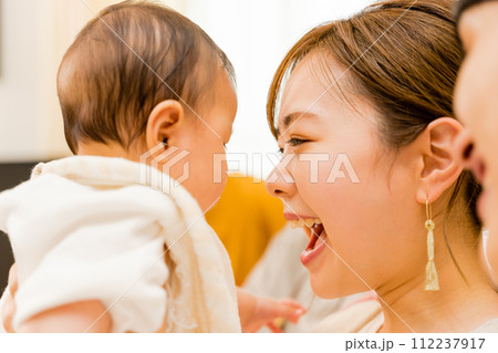 0歳の赤ちゃんをあやすために目を合わせようとする笑顔の母親とそれを見守る父親の3人の家族 112237917