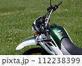 春の晴れた真昼の草原で上から太陽の強い光を受ける、停車しているオフロードバイク2 112238399