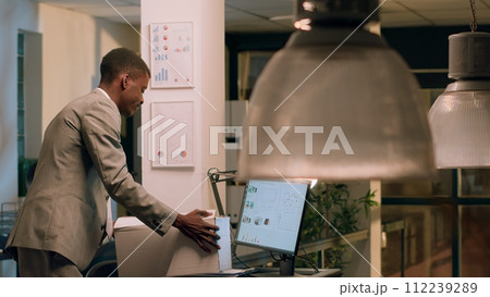 Sad african american employee packing desk belongings after being laid off from job after redundant staff reduction. Businessman putting office decorations in box after being fired Sad african american employee packing desk belongings after being laid off from job after redundant staff reduction. Businessman putting office decorations in box after being fired 112239289