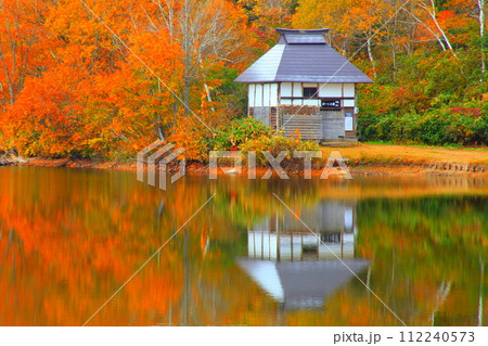 紅葉を映す湖面の小屋 112240573