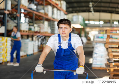 Young loader guy pushing cart in warehouse Young loader guy pushing cart in warehouse 112240943