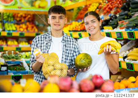 Family couple posing with purchases of vegetables and fruits in supermarket Family couple posing with purchases of vegetables and fruits in supermarket 112241337