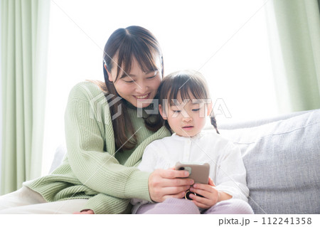 楽しくスマホを見る親子(母と娘）のイメージ　アプリや動画、ゲームを一緒に見る	 112241358