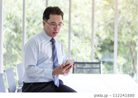 Business colleague working together using smartphone searching website and blogs for business news in conference room. Asian young man wear suit and tide formal dress waiting meeting. Business concept 112241880