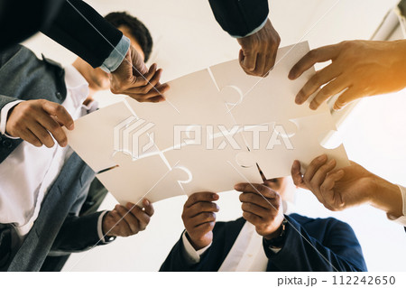 The concept of teamwork and partnership. Businessman's hands putting together puzzle pieces in the office and join together in a jigsaw puzzle team. Charity. Volunteers. Business unity as a team. The concept of teamwork and partnership. Businessman's hands putting together puzzle pieces in the office and join together in a jigsaw puzzle team. Charity. Volunteers. Business unity as a team. 112242650