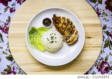 Top view of roasted chicken breast fillet steak with rice, vegetables salad and spicy sauce in white plate on wooden table.  Top view of roasted chicken breast fillet steak with rice, vegetables salad and spicy sauce in white plate on wooden table.  112242853