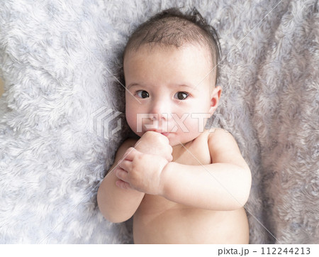 ふかふかのベッドの上で指しゃぶりをしているハーフの裸の男の子赤ちゃん ふかふかのベッドの上で指しゃぶりをしているハーフの裸の男の子赤ちゃん 112244213