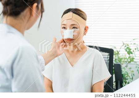 美容外科で整形手術を受けて術後に医師の診察を受ける女性（ダウンタイム・小顔整形・エラ削り・骨切り） 112244455