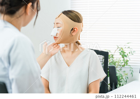 美容外科で整形手術を受けて術後に医師の診察を受ける女性（ダウンタイム・小顔整形・エラ削り・骨切り） 112244461